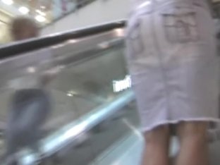 Leggy babe in short skirt riding on the escalator